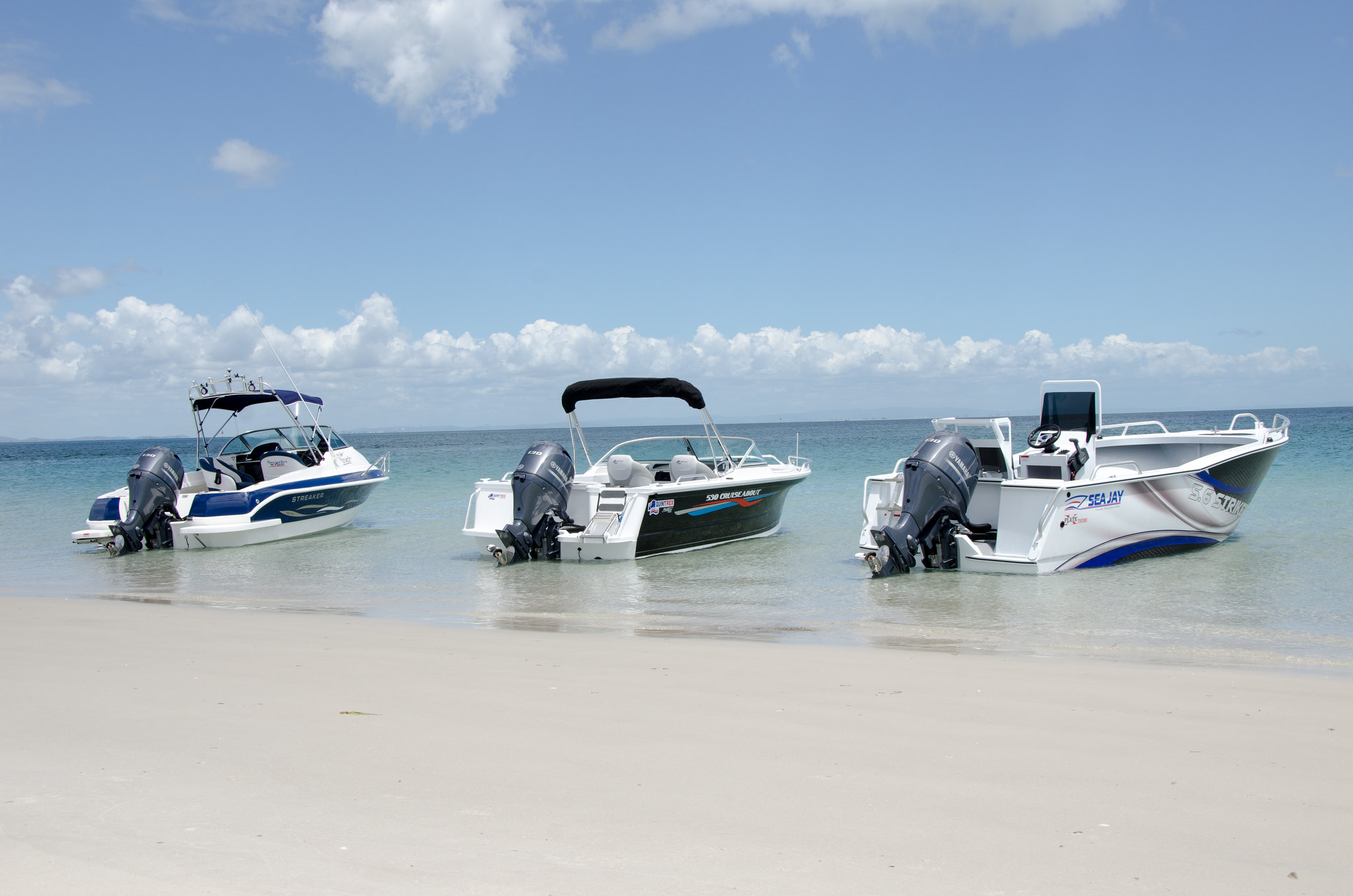Three open boats with outboard motors lined up ashore.