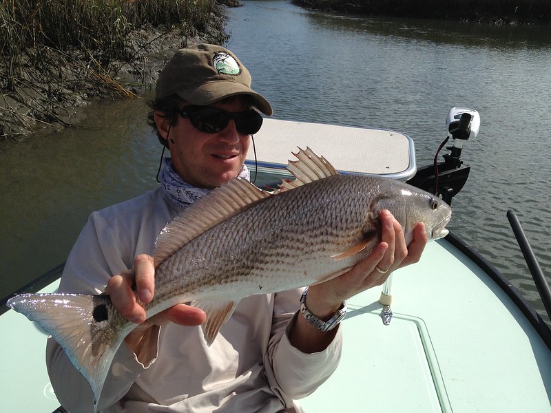 A man on a boat holding a fish he caught.