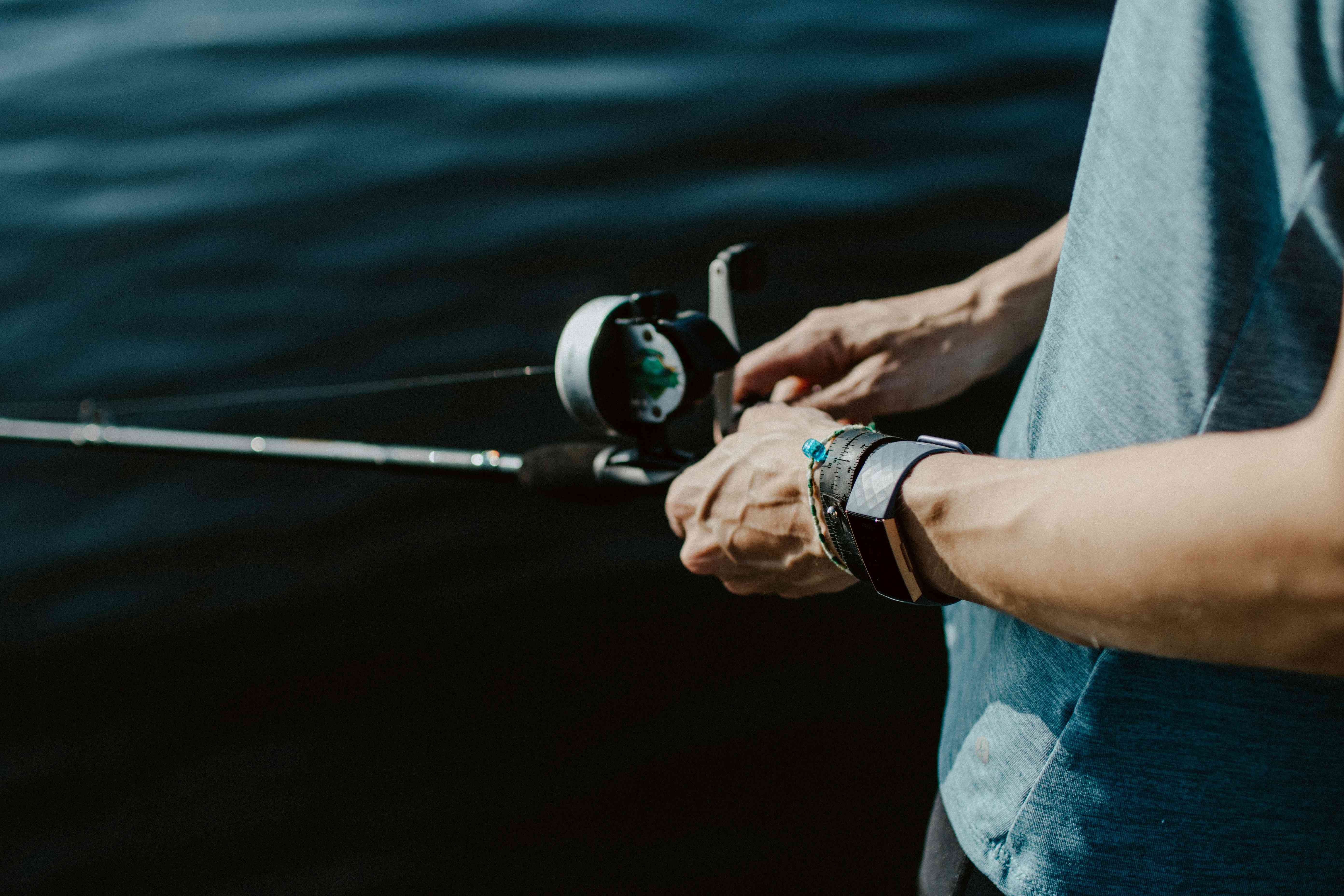 A man holding fiddling with a fishing reel while trying to lure in his catch.