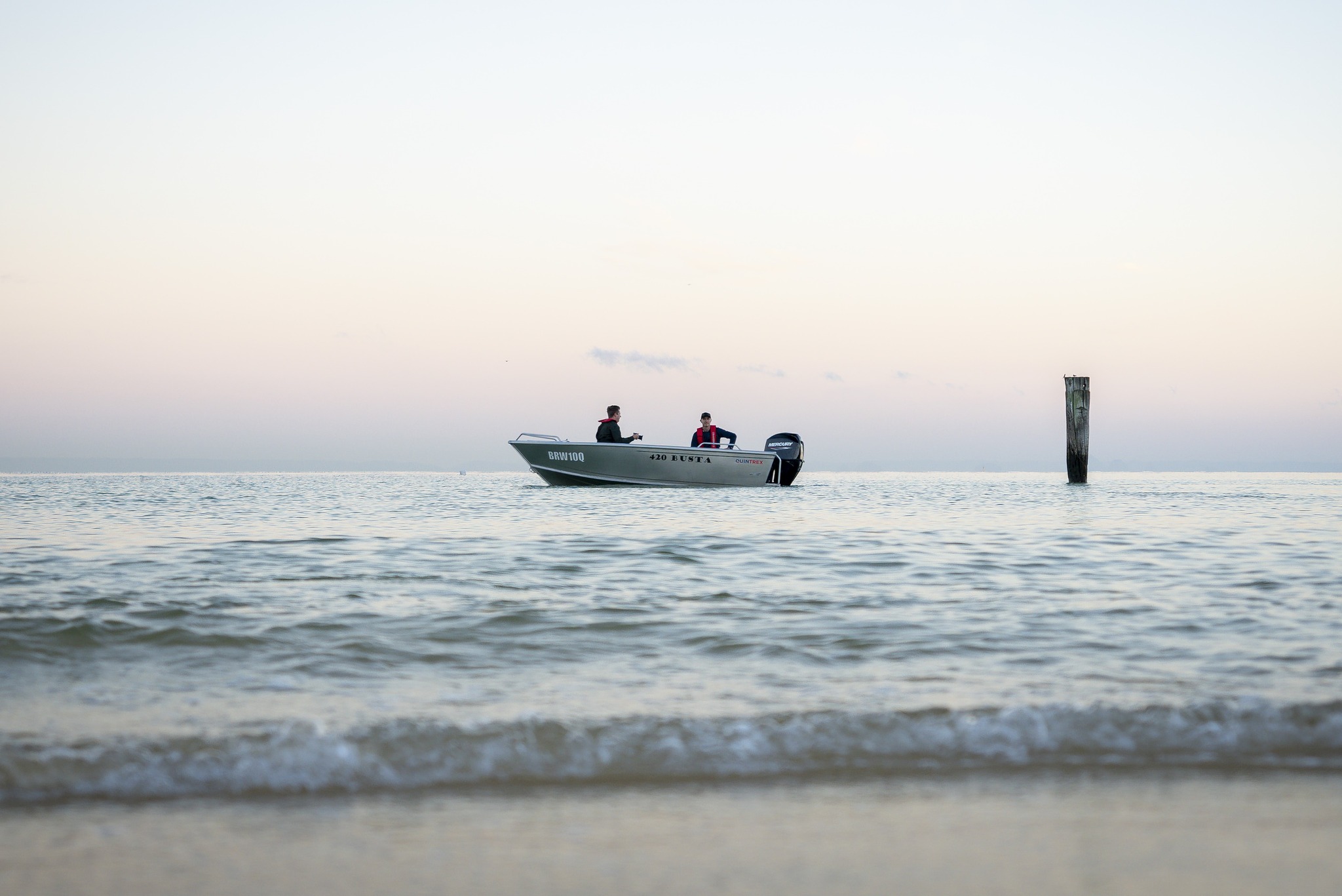two men onboard a Quintrex boat near the shore.
