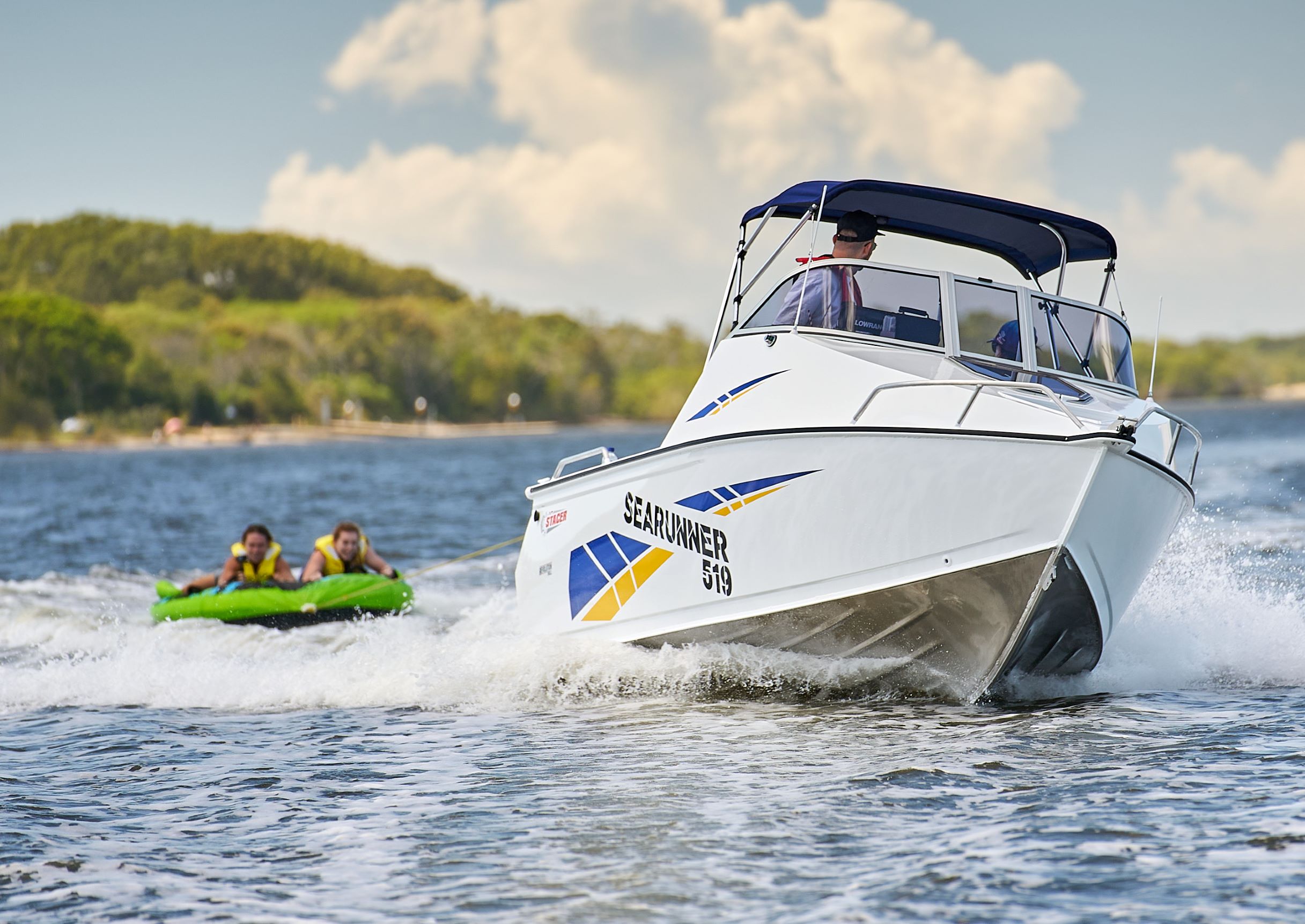 Two people on a tube being towed behind a Stacer Sea Master.